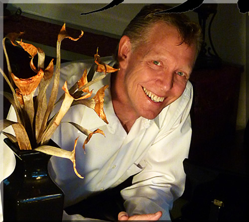 photo of Jerry Michelsen leaning on piano, smiling, with flowers